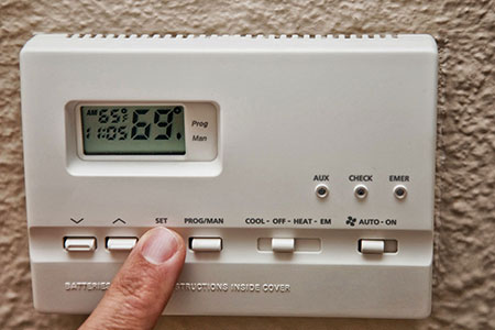 A person is pressing the temperature on an electronic thermostat.