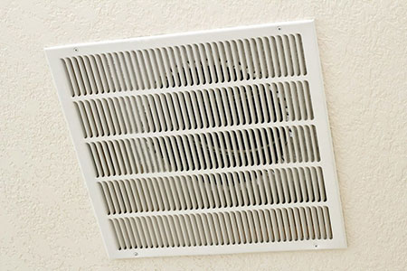 A white air vent on the side of a wall.