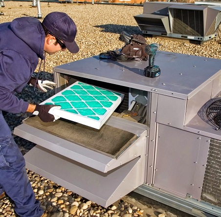 A man in purple jacket and hat working on an air conditioner.