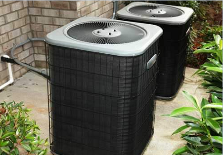 Two air conditioners are sitting outside on the ground.